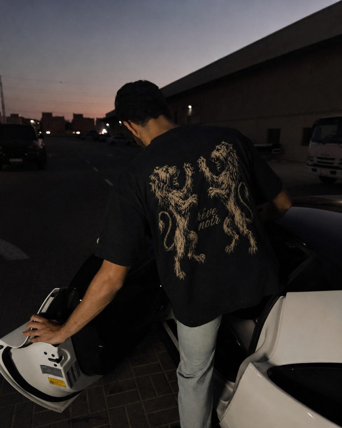 Herald tee at dusk beside a supercar